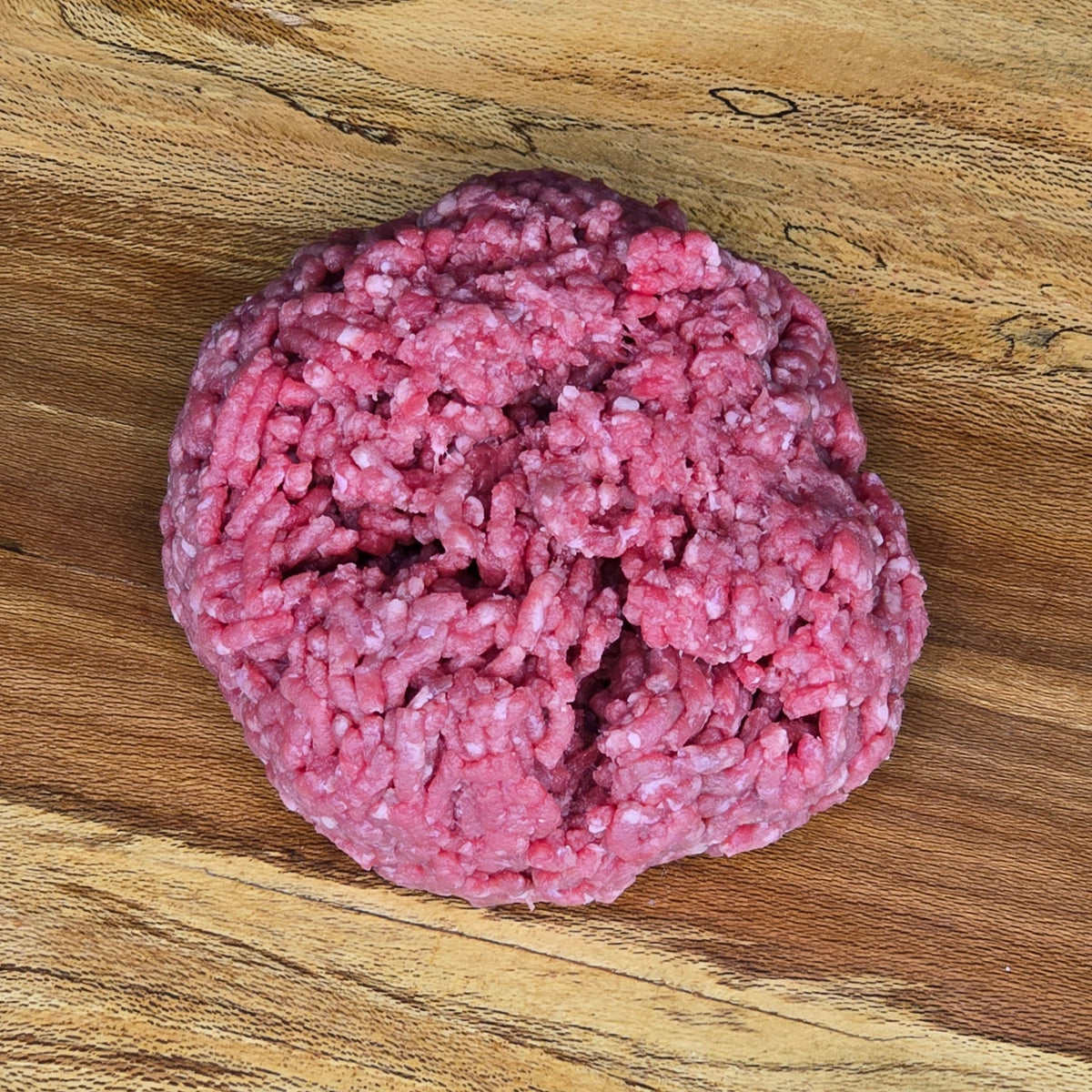 A raw ground beef hamburger patty on a wooden surface.