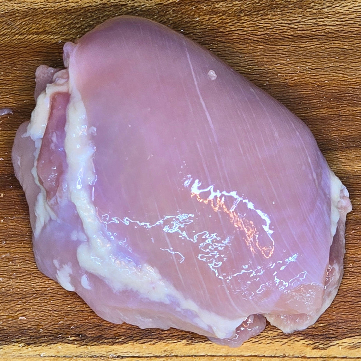 A single boneless skinless chicken thigh on a wooden cutting board.