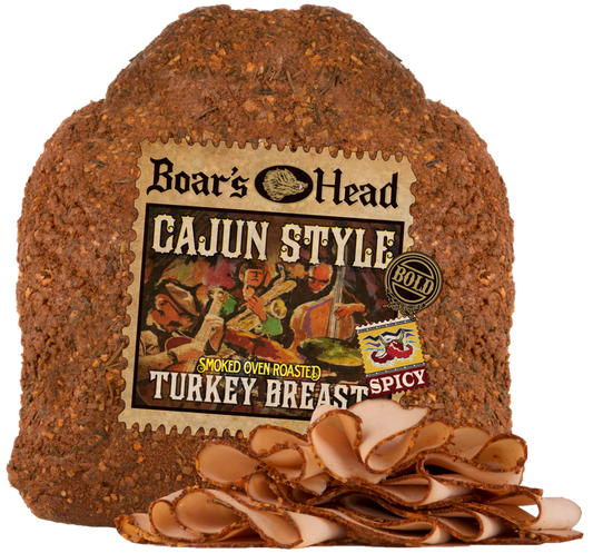 Boar's Head Cajun Style Smoked Oven Roasted Turkey Breast. The whole cured turkey loaf is shown with several slices cut and fanned out in front on a white background.